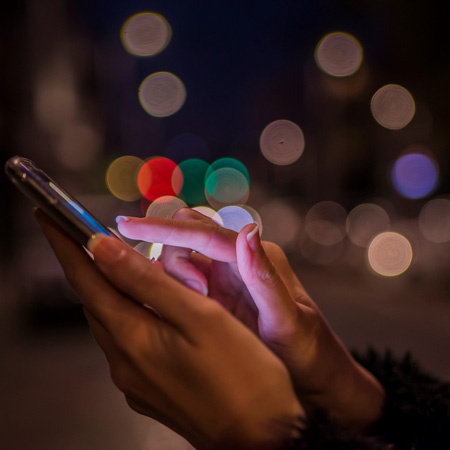 Woman using her mobile phone, city skyline night light background